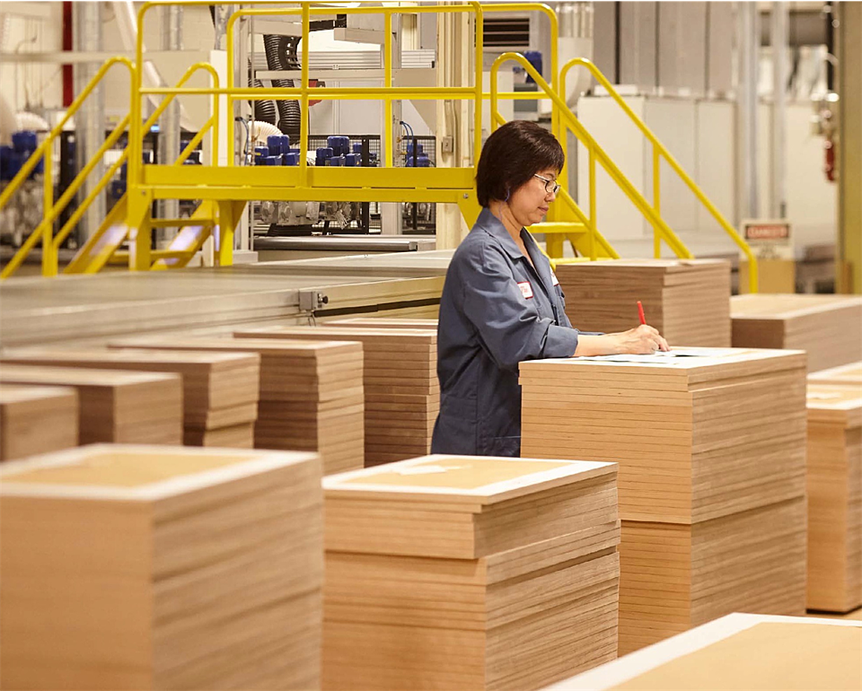 Worker inspecting stacked wood panels in a manufacturing facility.